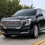 A black 2024 GMC Terrain Denali driving on an open road.