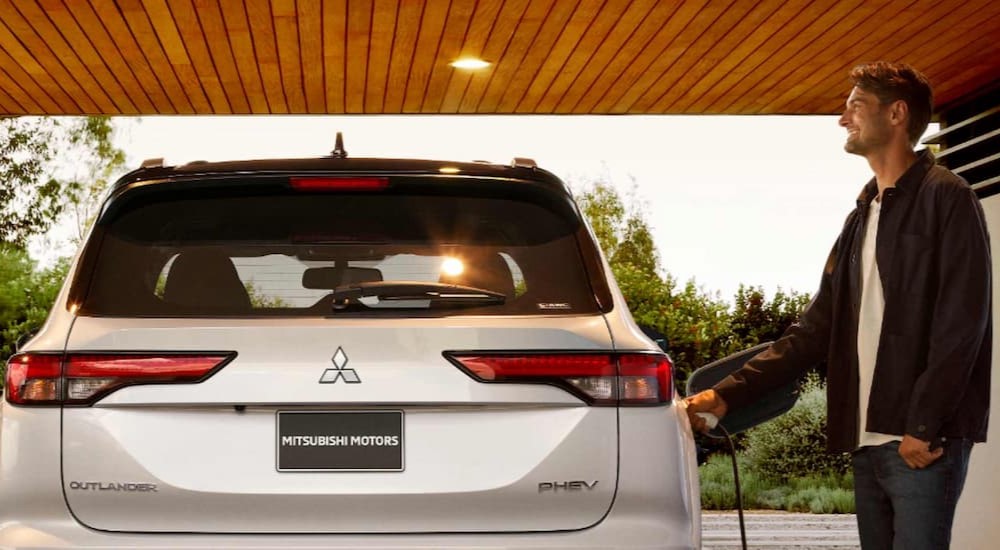 A person is shown charging a white 2025 Mitsubishi Outlander PHEV.