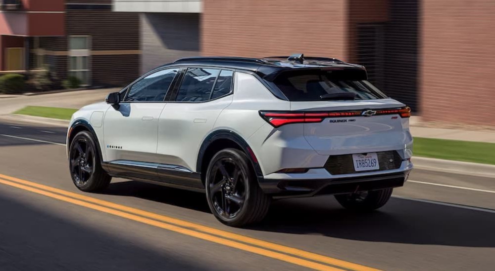 A white 2025 Chevy Equinox RS EV is shown driving to a Chevy dealer.