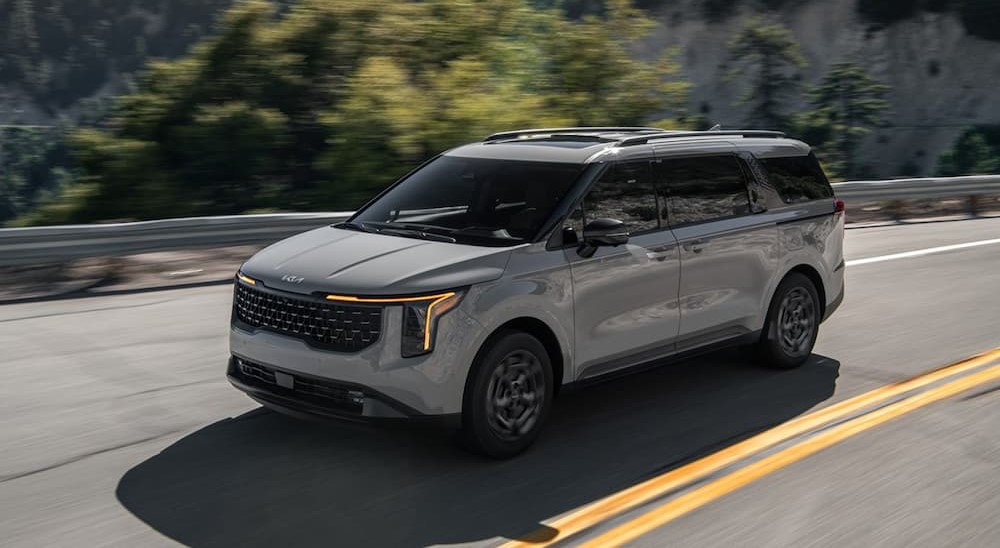 A gray 2025 Kia Carnival is shown driving to visit a Kia dealer.