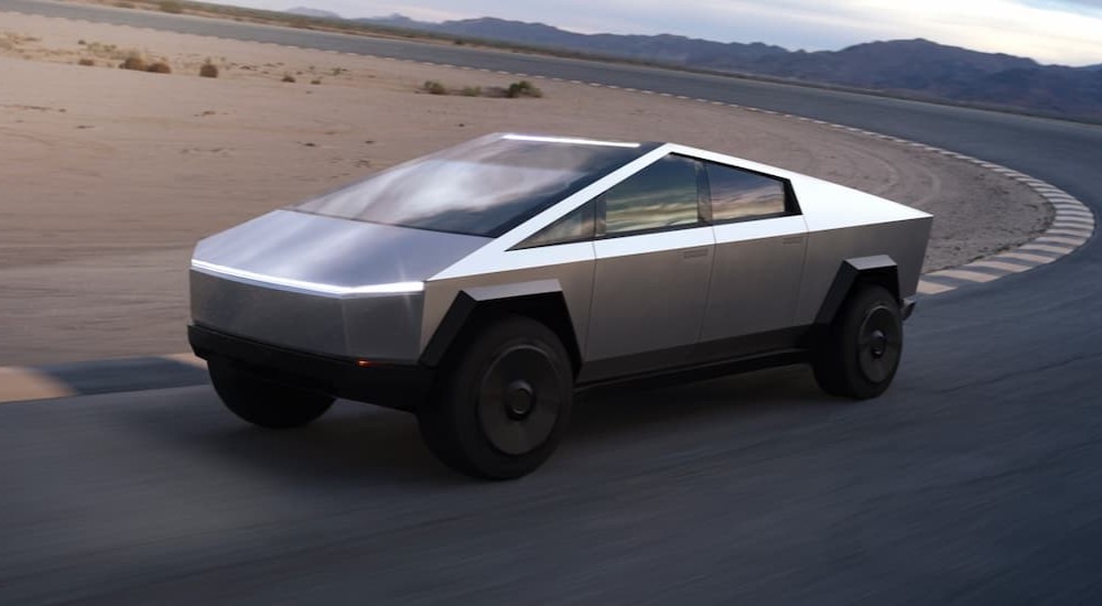 A silver 2024 Tesla Cybertruck is shown driving on a racetrack. 