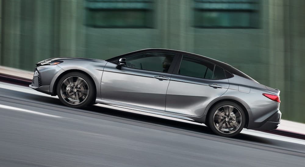 Side angle view of a grey 2025 Toyota Camry driving in a city.