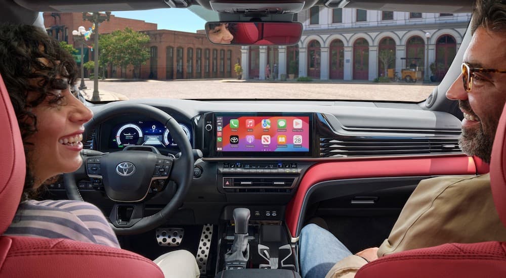 Two people sitting in the front seat of the black and red interior of a 2025 Toyota Camry.