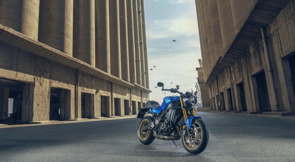 A blue 2023 Yamaha XSR900 is shown parked in an alleyway.