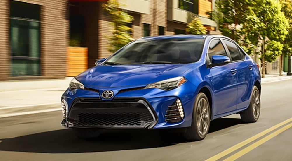 A blue 2019 Toyota Corolla is shown driving near a brick building.