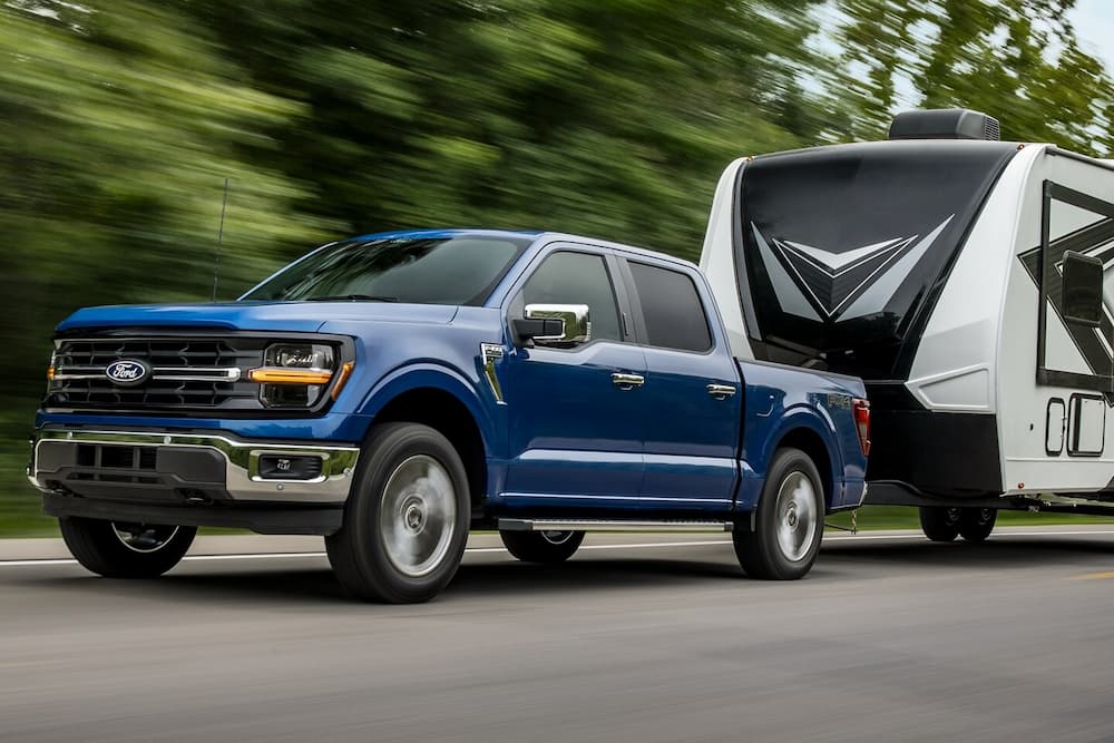 A blue 2024 Ford F-150 King Ranch is shown towing a trailer after viewing a Ford F-150 for sale.