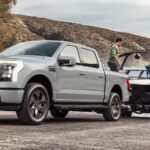 A silver 2024 Ford F-150 Lightning for sale is shown towing a boat.