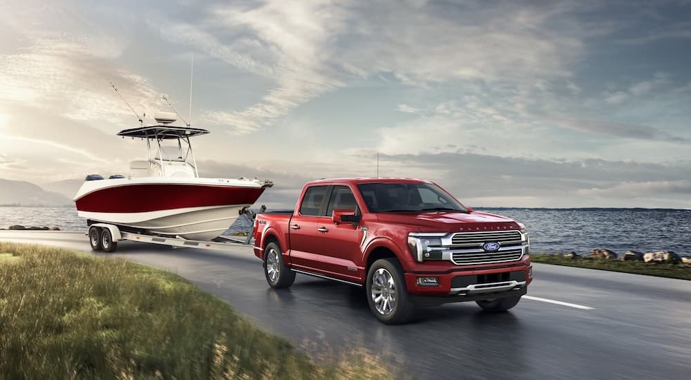 A red 2024 Ford F-150 Platinum is shown towing a boat to view trucks for sale.