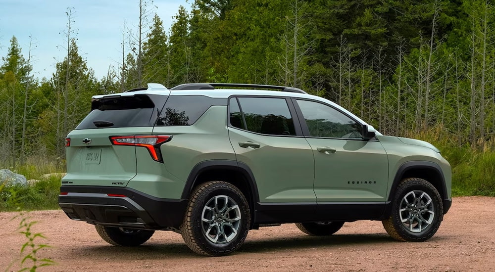 Rear view of a green 2025 Chevy Equinox ACTIV parked in a wooded clearing after leaving a Chevy dealer.