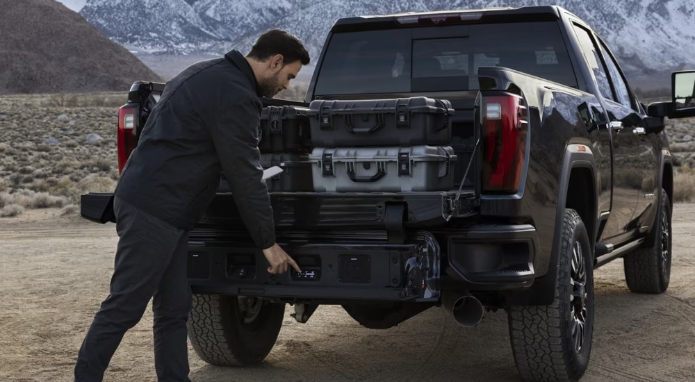 A man lowering the MultiPro tailgate on a black 2025 GMC Sierra 2500 HD for sale.