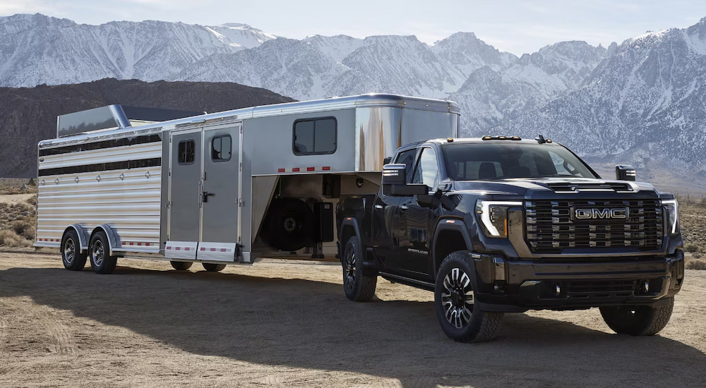 A black 2025 GMC Sierra 2500 HD Denali towing a large trailer.