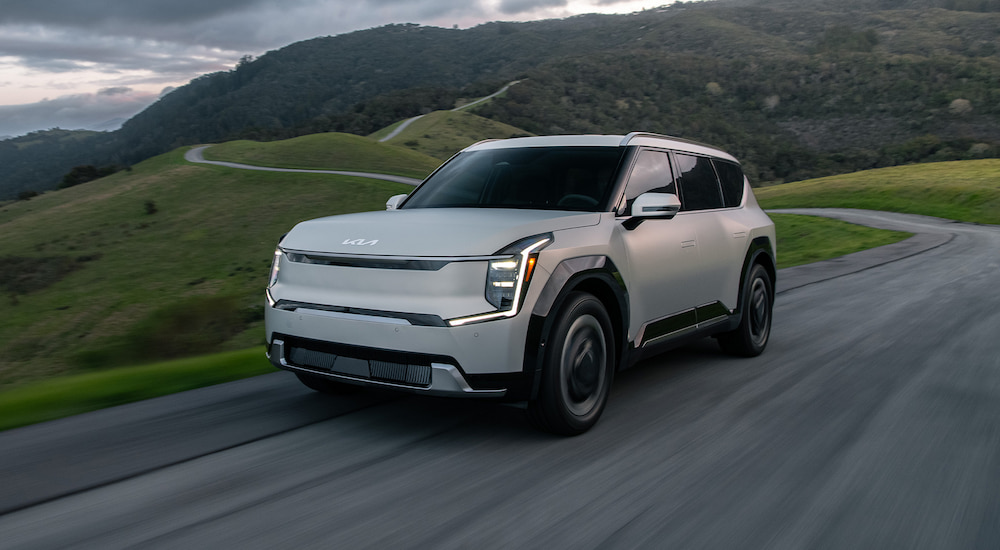 A pearl white 2024 Kia EV9 driving on a hilly road.