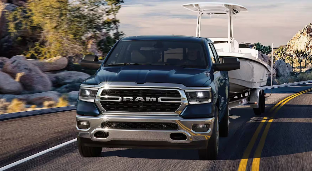 Head-on view of a black 2024 Ram 1500 Big Horn towing a boat on the highway.