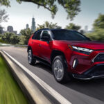 A red 2025 Toyota RAV4 PHEV driving from a Toyota dealer.