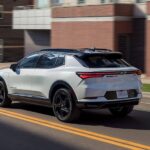 A white 2025 Chevy Equinox RS is shown driving on a city street.