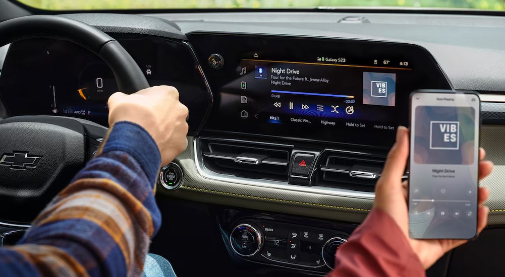 A person is shown using a phone to connect to the infotainment center in a 2025 Chevy Trailblazer for sale.