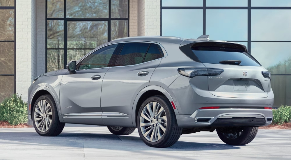 Rear view of a silver 2024 Buick Envision Avenir parked at a dealership with cars for sale.