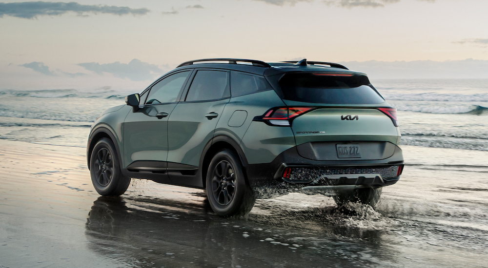 Rear view of a grey-green 2025 Kia Sportage X-Pro Prestige driving on a beach.