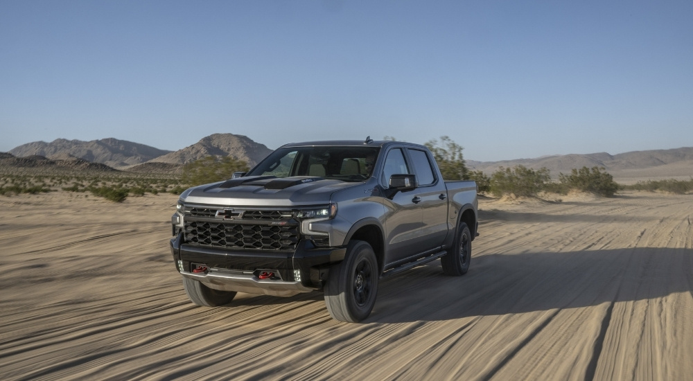 A silver 2023 Chevy Silverado 1500 ZR2 driving on sand after viewing used Chevy trucks for sale.