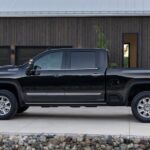 A black 2025 Chevy Silverado 2500 High Country is shown parked near a Chevy dealer.