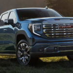 A blue 2025 GMC Sierra 1500 Denali parked on a grassy hill.