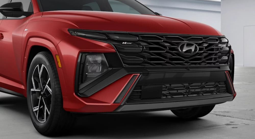 A close-up of the grille is shown on a red 2025 Hyundai Tucson HEV N-Line.