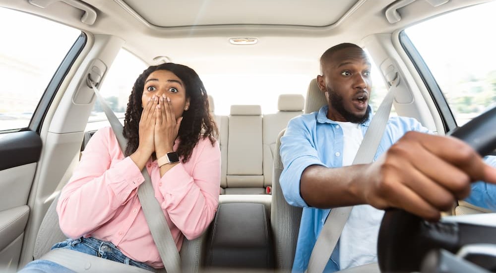 Two people are shown driving a vehicle in shock.