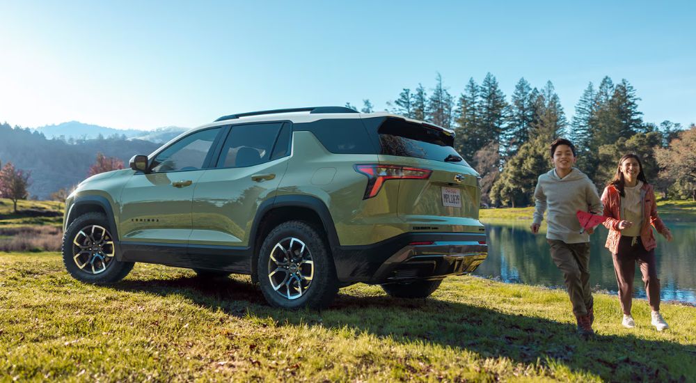 Kids running near a green 2025 Chevy Equinox ACTIV parked near a pond.