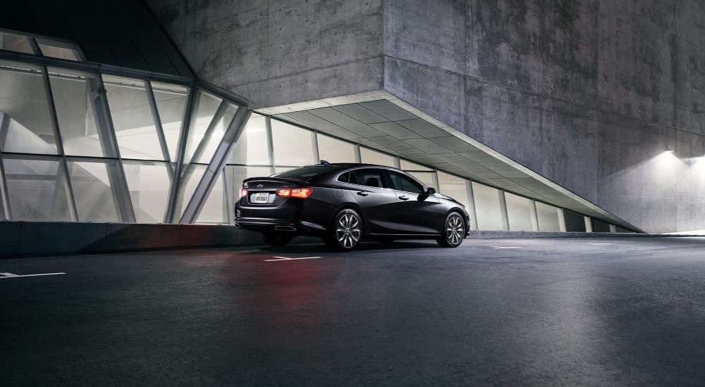 Rear view of a black 2024 Chevy Malibu RS parked outside a building.