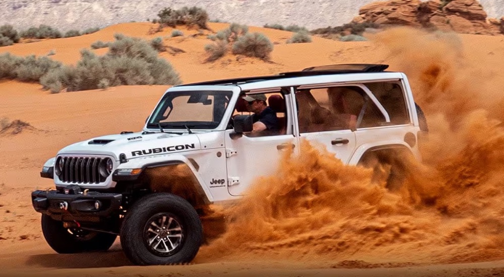 A white 2025 Jeep Wrangler Rubicon kicking up sand while off-roading.