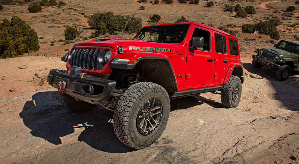 A red 2025 Jeep Wrangler Rubicon off-roading up a rocky trail.