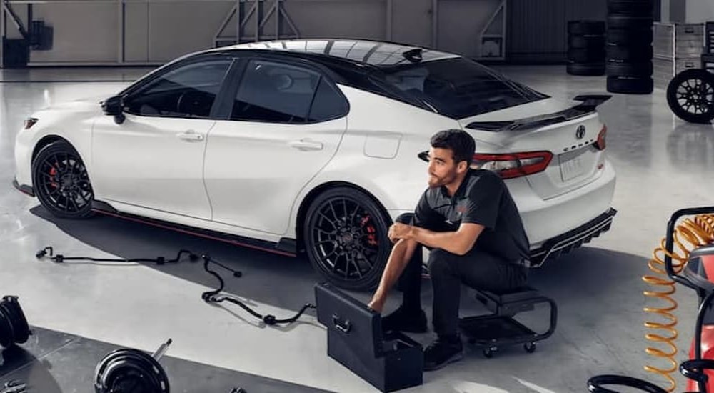 A technician is shown sitting near a white 2022 Toyota Camry TRD.