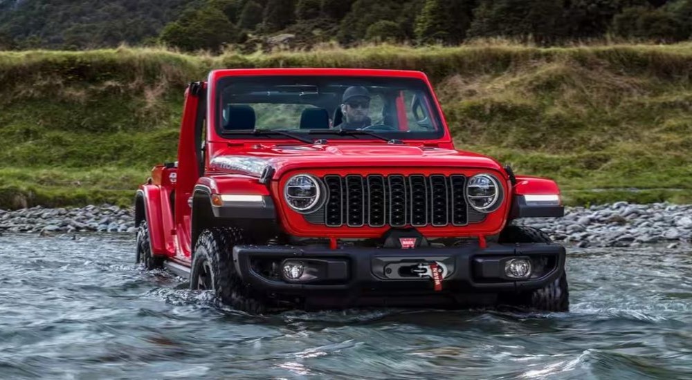 A red 2024 Jeep Wrangler Rubicon Unlimited is shown driving through a stream after viewing used cars for sale in Colorado Springs.