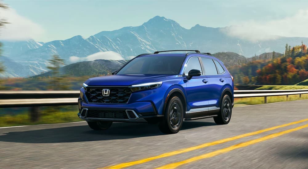 A blue 2025 Honda CR-V Hybrid Sport Touring is shown driving on a highway.