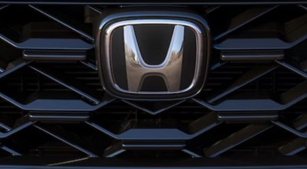 A close-up of the grille and badge are shown on a 2025 Honda CR-V Hybrid Sport Touring.