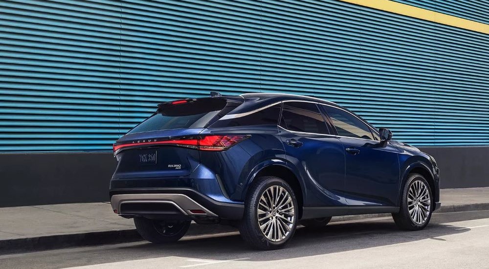 A blue 2023 Lexus RX 350 car for sale is parked next to a blue wall.