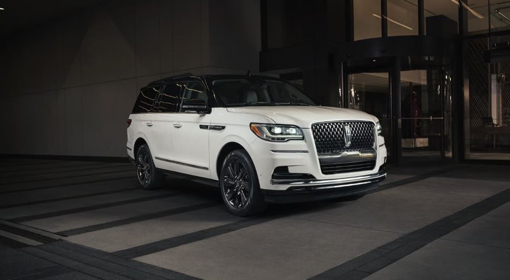 A white 2023 Lincoln Navigator is parked outside of a tall building at night.