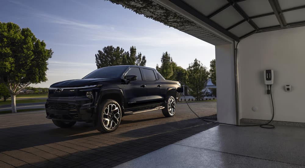 A black 2025 Chevy Silverado EV is parked near a garage entrance while charging.