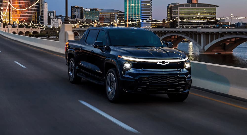 A black 2025 Chevy Silverado EV RST for sale is driving on a bridge in a city.