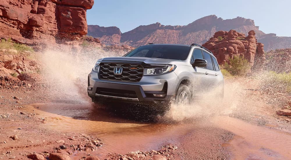 A grey 2025 Honda Passport TrailSport driving over a shallow puddle.