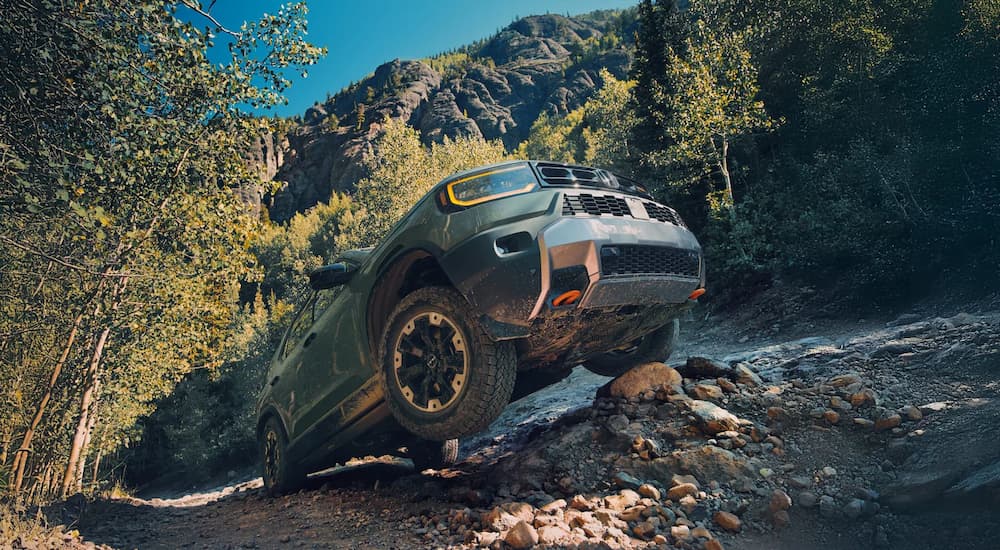 Low angle view of a green 2025 Honda Passport TrailSport driving off-road up a hill.