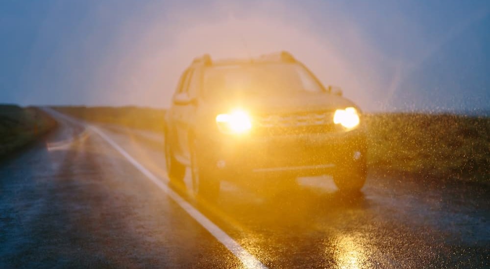 A vehicle is shown driving with headlights on.