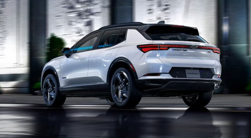 A white 2024 Chevy Equinox EV is shown driving on a city street.