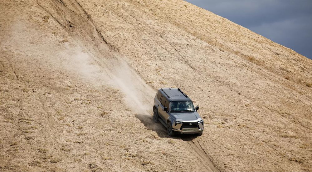 A silver 2025 Lexus GX 550 Overtrail off-roading down a long sandy hill.