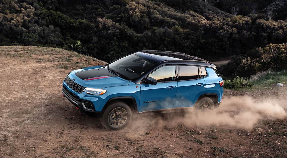 A blue 2025 Jeep Compass Trailhawk kicking up dust while driving off-road from a dealer with a Jeep Compass for sale.