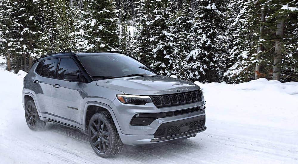 A grey 2025 Jeep Compass Trailhawk driving down a snowy road.