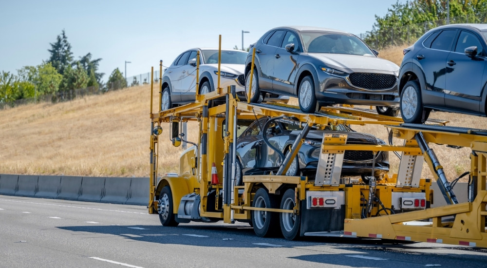 Vehicles are shown being shipped on a yellow transport truck.